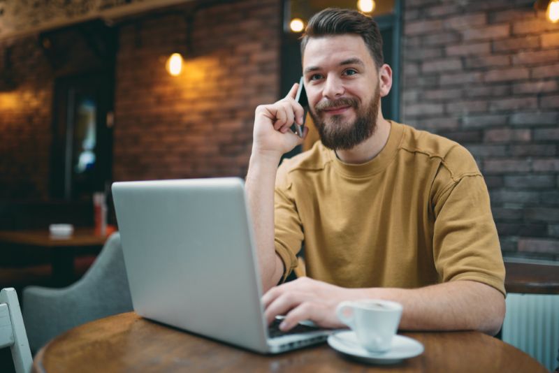 Man working on laptop and making a phone call from a coffee shop