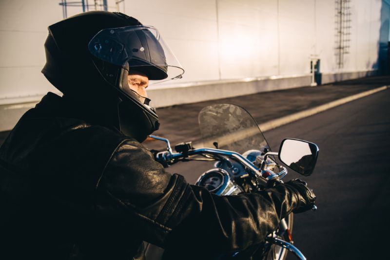 A man wearing all black riding a motorcycle at sunset